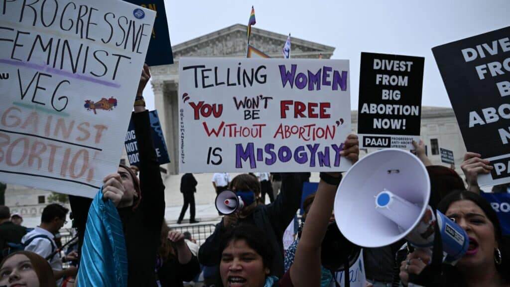 Protesters outside the Supreme Court holding signs advocating for abortion rights and shouting through a megaphone.