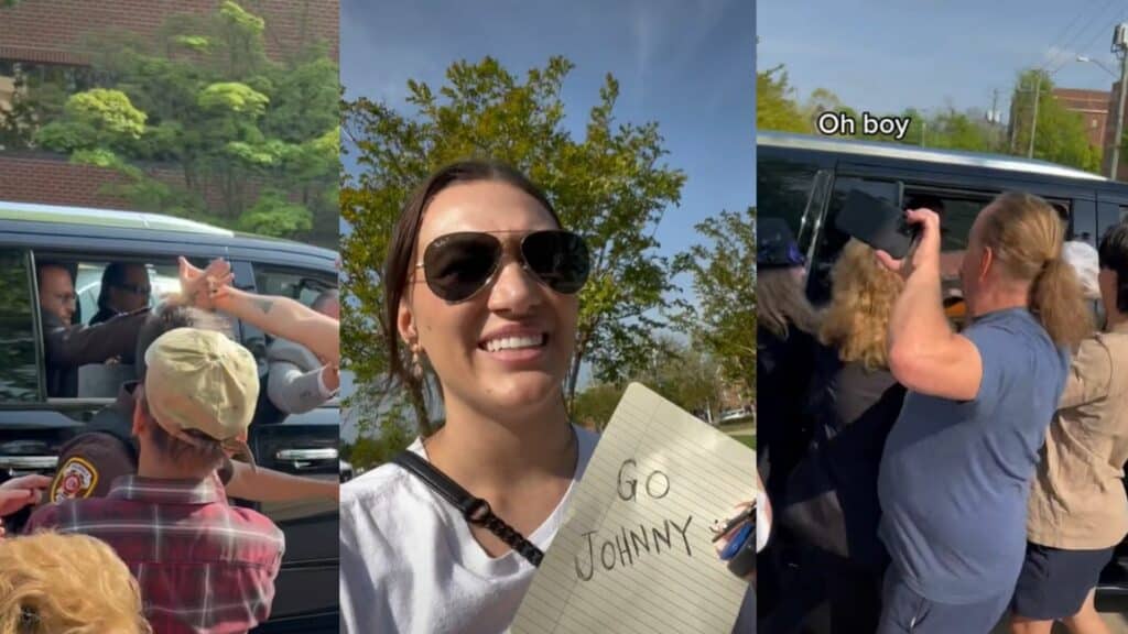 Woman wearing sunglasses holding a "Go Johnny" sign smiling outdoors among a crowd near a black vehicle