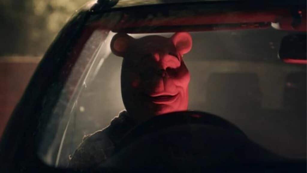 Person wearing a red bear mask sitting behind the steering wheel of a car at night