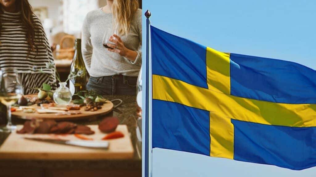 Two people enjoying wine and snacks indoors next to a Swedish flag waving outside against a clear sky