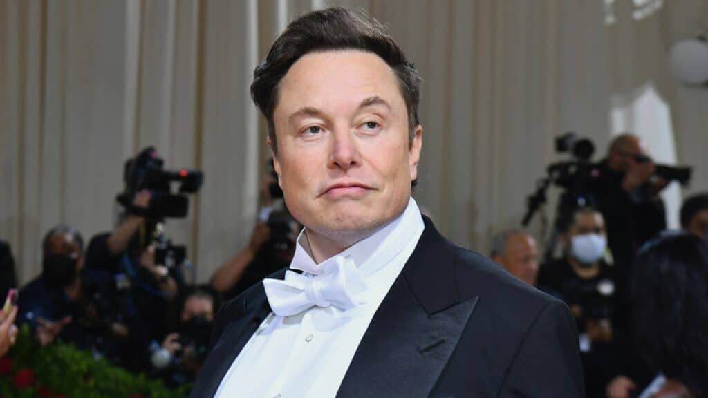 Elon Musk wearing a white bow tie and black tuxedo at a formal event with photographers in the background.
