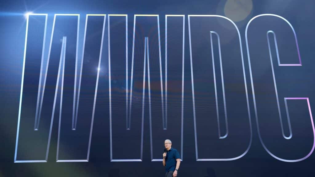 Tim Cook speaking on stage in front of a large "WINDOS" sign with a dark blue background.