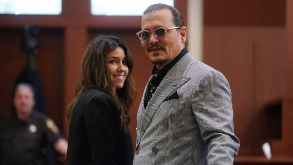 Johnny Depp wearing sunglasses and a gray plaid suit standing next to a smiling woman in a courtroom.