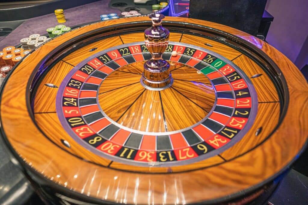 Wooden roulette wheel with a white ball near number 12 and stacks of colorful casino chips nearby