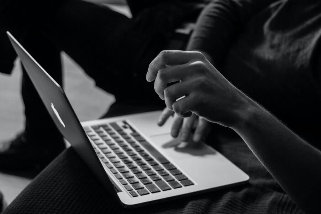 Person using a MacBook laptop with one hand poised above the keyboard in black and white.