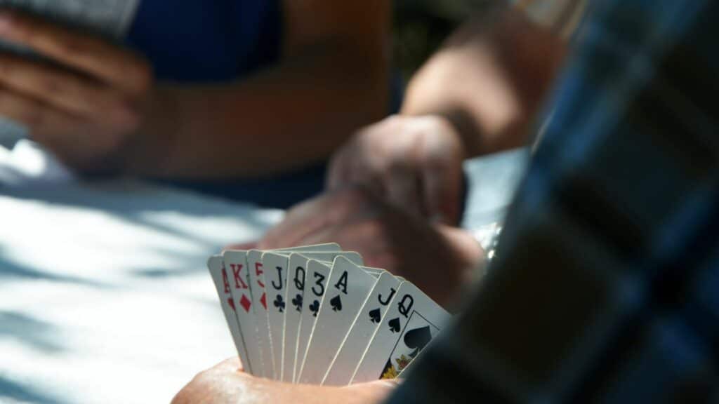 Person holding a hand of playing cards including Ace, King, Queen, Jack, and 3 of various suits during a card game