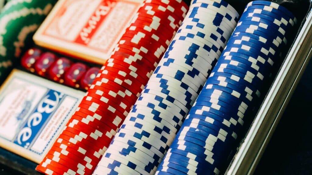 Stacks of red, white, and blue poker chips with Bee playing cards and red dice in a poker set case
