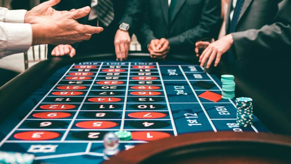 People placing bets and handling chips at a roulette table in a casino setting.