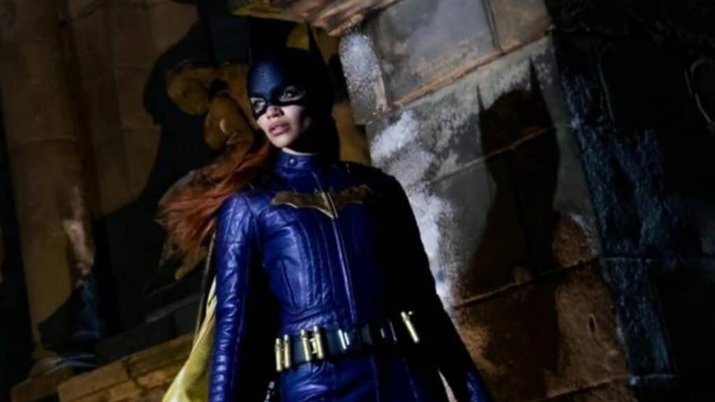 Batwoman in blue leather suit and mask standing against a stone wall at night