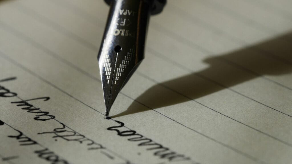 Close-up of a fountain pen writing cursive text on lined paper with a shadow cast to the right.