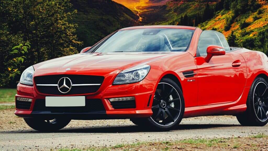 Red Mercedes-Benz convertible sports car parked on a mountain road with greenery and hills in the background.
