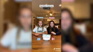 Two girls, Lauren and Mattie, sitting at a table with a quiz card reading "Largest Country by Population" during a quiz show challenge.