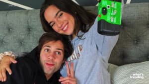 Two people smiling and taking a selfie with a green disposable camera on a gray couch