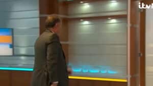 Man in a suit walking away in a modern TV studio with ITV News logo visible