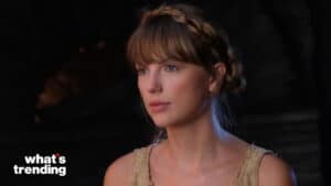 Taylor Swift with braided hair and beige sleeveless top in a dimly lit setting