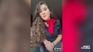 Young woman with long curly hair wearing a black shirt and red scarf speaking in a TikTok video.