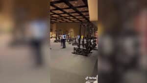 Workers assembling black weightlifting racks in a large indoor gym or fitness facility