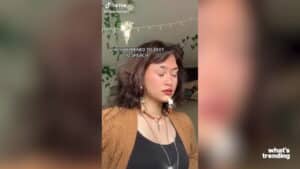 Young woman with curly hair and brown cardigan posing with eyes closed in a decorated room, TikTok @wannabe.fairy