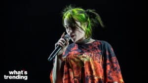 Billie Eilish singing on stage with green hair and a graphic orange and black shirt