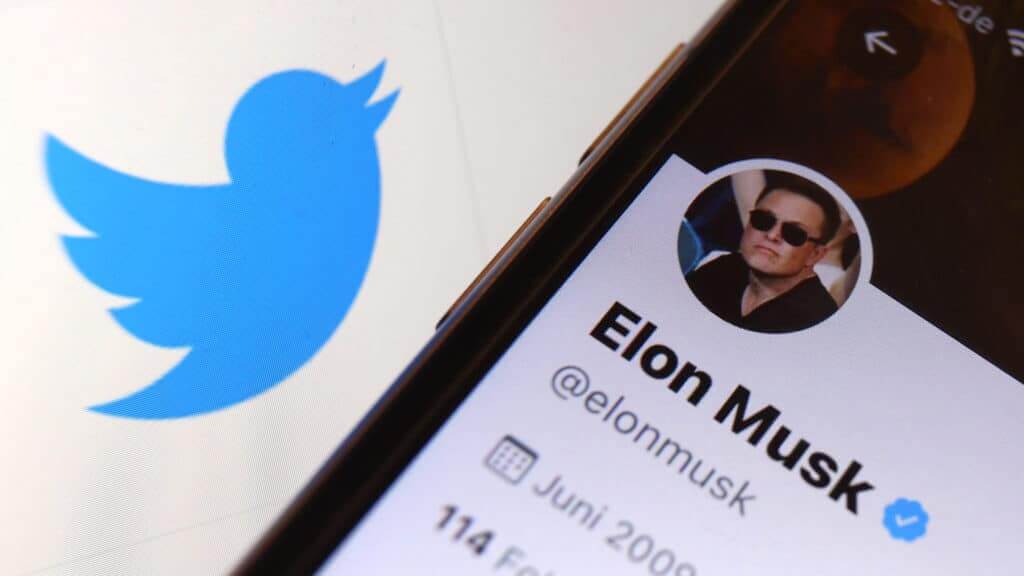 Close-up of Elon Musk's verified Twitter profile on a smartphone next to the Twitter logo.