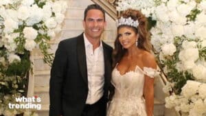 Man in black tuxedo and woman in white wedding dress with tiara posing in front of floral staircase backdrop