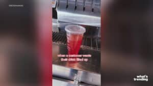 Plastic cup filled with red drink and sealed with a plastic lid on a metal counter near a drink dispenser