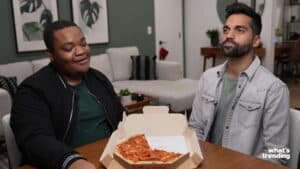 Two men sitting at a table with a partially eaten pepperoni pizza in a cardboard box in front of them