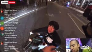 Person sitting on the ground at night on a street, appearing distressed, with live chat comments and a small inset of a man speaking.