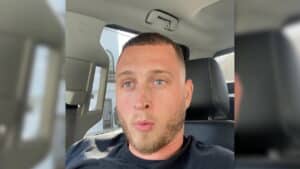 Man with short hair and beard sitting in a car seat, looking slightly to the side.