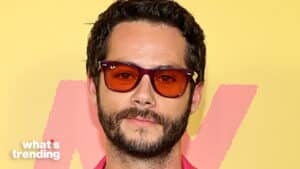 Man with dark hair and beard wearing red-tinted Ray-Ban sunglasses against a yellow and pink background