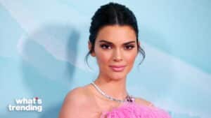 Kendall Jenner wearing a pink feathered dress and silver necklace against a blue background