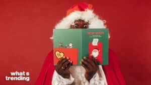 Person dressed as Santa Claus holding a green "Dear Santa" card with red background and "what's trending" text