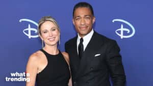 Two people posing in front of a Disney backdrop, a woman in a black dress and a man in a black suit and tie.