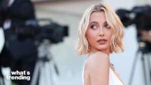 Blonde woman in white dress looking over her shoulder at an event with cameras in the background