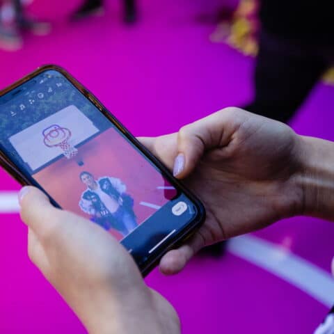 Person holding smartphone showing video of another person standing under a basketball hoop on a pink court with "what's trending" text visible