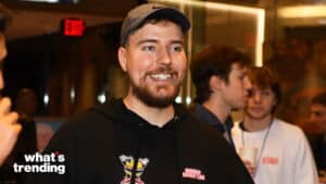 Smiling man wearing a black "Beef's Burger Team" hoodie and Nike cap at a social event with people in the background