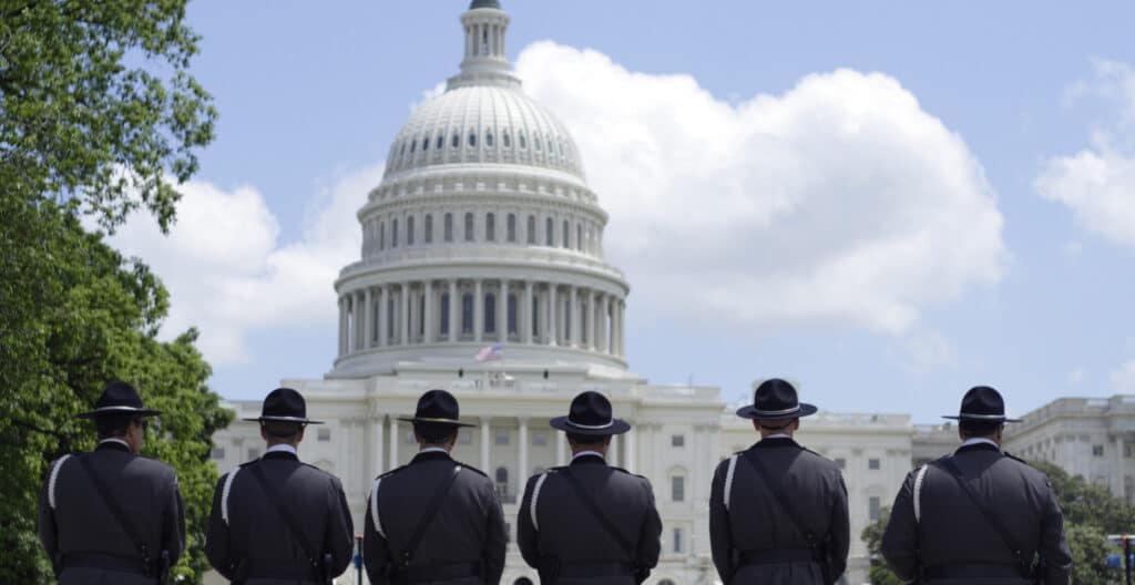 Six uniformed officers standing with their backs to the camera in front of the U.S. Capitol building