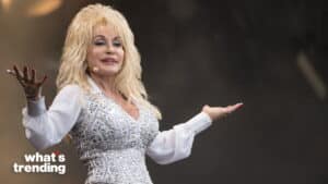 Dolly Parton performing on stage wearing a white embellished outfit with arms outstretched
