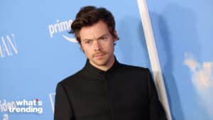 Harry Styles wearing a black jacket at a Prime Video event with a blue backdrop.