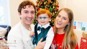 Smiling family with a young red-haired child in glasses and a green vest in front of a decorated Christmas tree