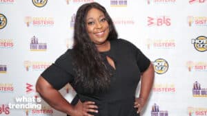Smiling woman in black dress posing with hands on hips at Circle of Sisters event backdrop