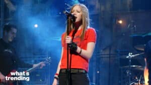 Avril Lavigne singing on stage wearing a red shirt with a guitarist in the background and "what's trending" text.