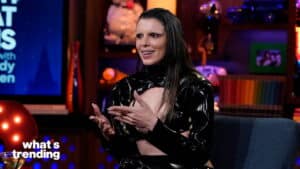 Person in a black cut-out latex outfit speaking on a talk show set with "what's trending" text visible.