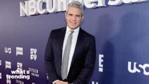 Andy Cohen in a pinstripe suit and gray tie at an NBCUniversal event with network logos on the backdrop