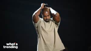 Kanye West holding a microphone above his head with eyes closed against a dark background