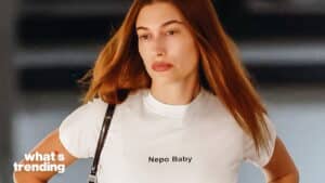 Woman with long red hair wearing a white "Nepo Baby" t-shirt and carrying a black strap bag