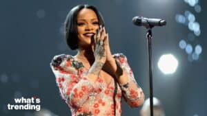Rihanna smiling and clapping on stage wearing a floral dress with a microphone in front of her