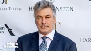 Alec Baldwin wearing a navy suit and striped tie at a red carpet event.