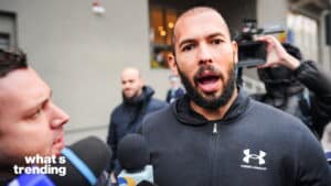 Man in Under Armour jacket speaking to reporters with microphones and a camera operator in the background