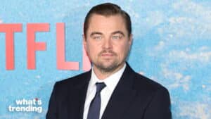 Leonardo DiCaprio in a dark suit and tie at a Netflix event with a blue and red backdrop.